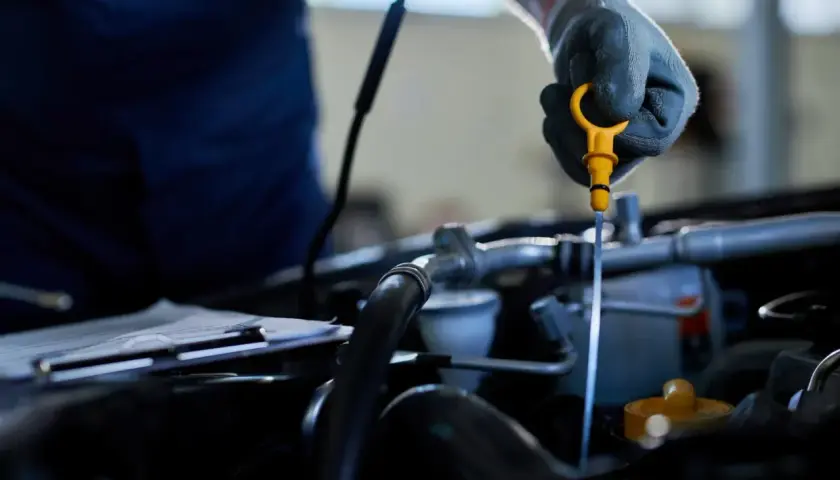 Mechanik w rękawiczce wyciąga bagnet, sprawdzając poziom oleju. To kluczowy element dbania o silnik, podobnie jak sprawny odma separator oleju.