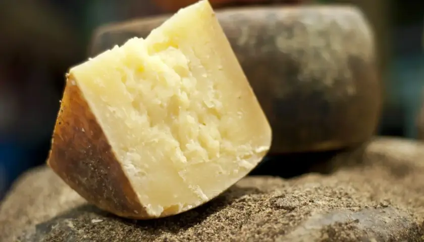 Kawałek twardego, żółtego sera, idealnego do pesto, leży na kamieniu obsypanym pieprzem.