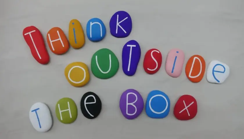 Kolorowe kamienie z literami tworzą napis "THINK OUTSIDE THE BOX". To jak polskie przysłowia po angielsku, zachęcające do nieszablonowego myślenia.
