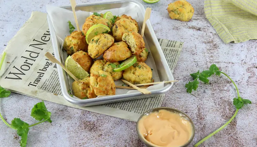 Plateau de délicieux accras dorés, garnis de quartiers de citron vert et de coriandre fraîche, servis avec une sauce crémeuse.
