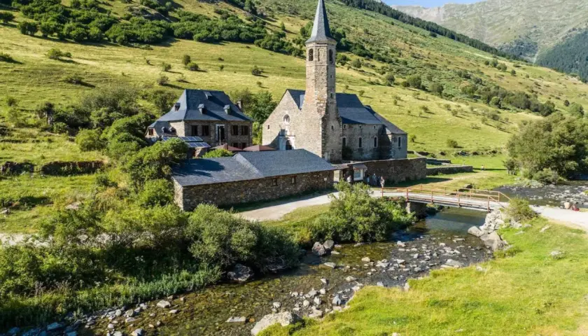 El santuari de Montgarri, una joya arquitectónica de piedra, se alza sereno junto a un arroyo cristalino, rodeado de verdes laderas montañosas.