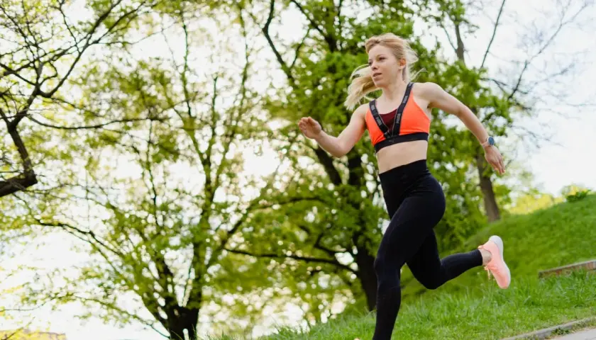Młoda kobieta w sportowym stroju biegnie po ścieżce w parku. To świetny sposób na rozpoczęcie przygody z bieganie dla początkujących.