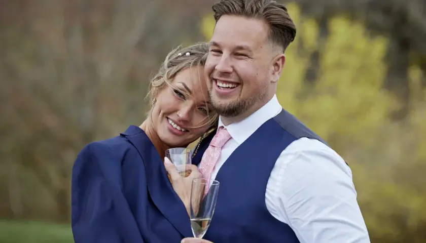 Ett lyckligt par, som från Love is Blind, firar med champagne. Rasmus ler stort, hans partner lutar sig mot honom.