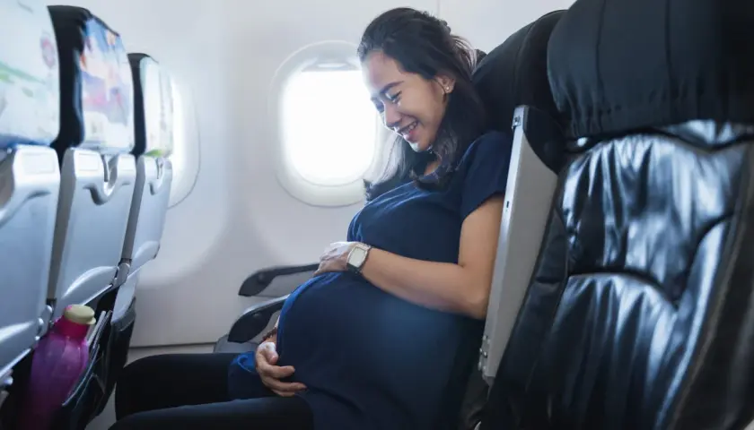 Glad gravid kvinna ler och håller sin mage medan hon sitter i ett flygplan.