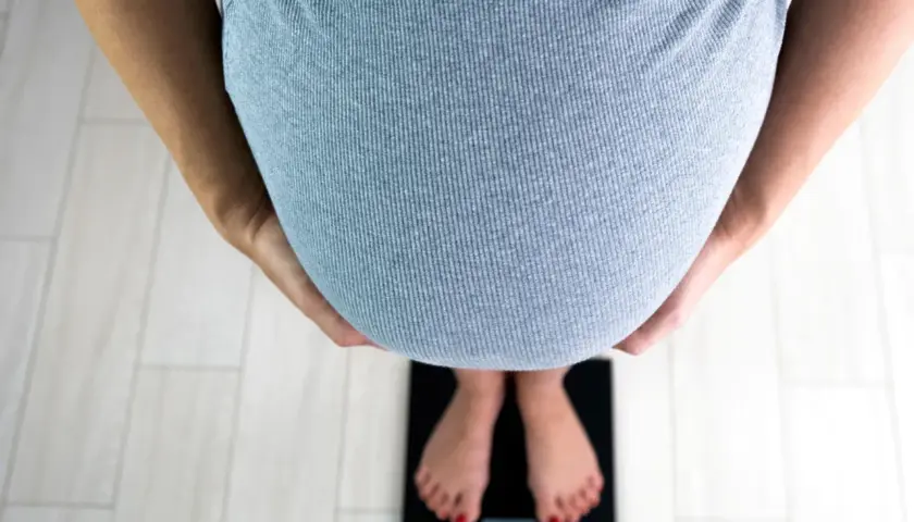 Kobieta w ciąży stoi na wadze. Zdjęcie może być inspiracją do poszukiwania informacji, jak zatrzymać przyrost wagi w ciąży.