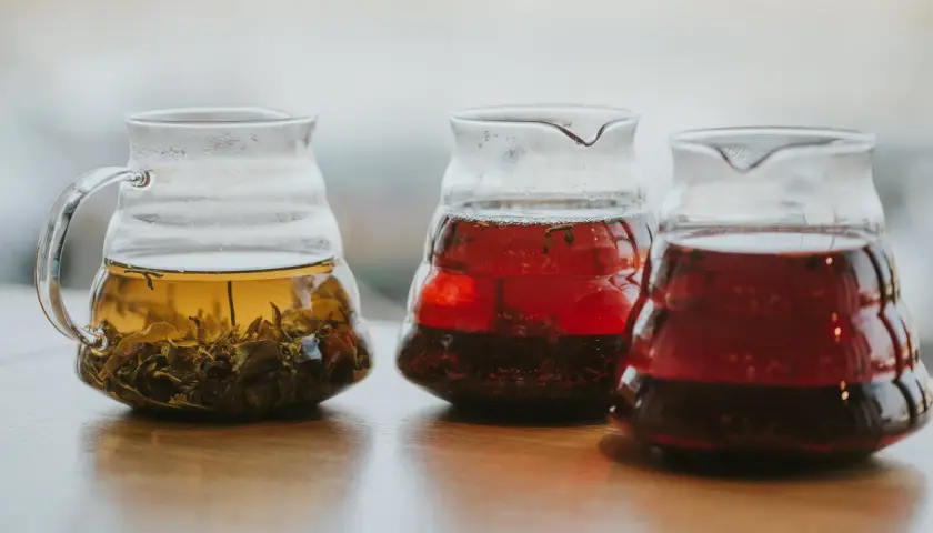 Trzy szklane dzbanki z zaparzonymi herbatami: jasnożółtą z liśćmi, czerwoną i ciemnoczerwoną, być może lapsang souchong.