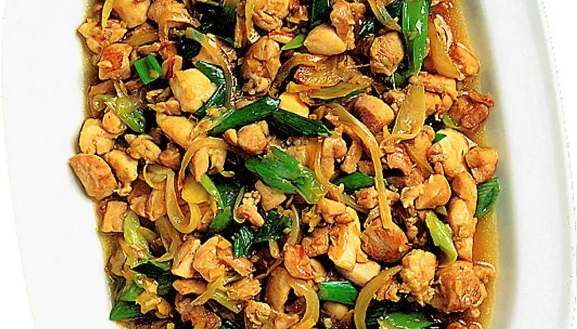 En närbild av en skål med saftig kyckling citrongräs, wokad med lök och gröna lökar.