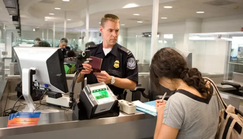 Funkcjonariusz sprawdza paszport kobiety przy stanowisku check-in na lotnisku.