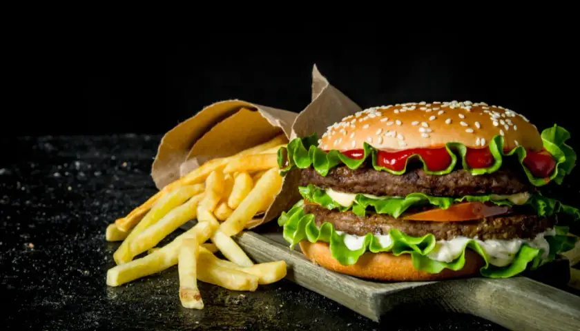 Podwójny hamburger z frytkami na ciemnym tle.