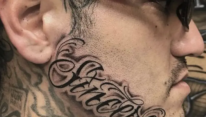 Wyrazisty tatuaż na twarzy z napisem "Sincere" w ozdobnej czcionce.