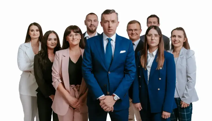 Grupa profesjonalistów w garniturach i kostiumach, stojąca przed białym tłem.