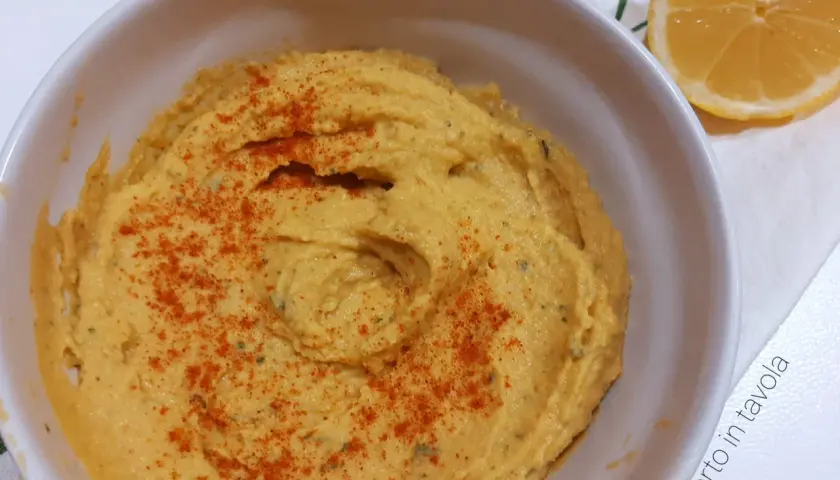 Hummus di ceci senza tahina, cremoso e spolverato di paprika, pronto per essere gustato con una fetta di limone.