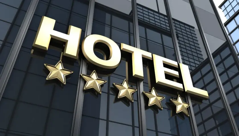 Złoty napis HOTEL i pięć gwiazdek na nowoczesnym, szklanym budynku. To zapowiedź luksusowego hotelu.