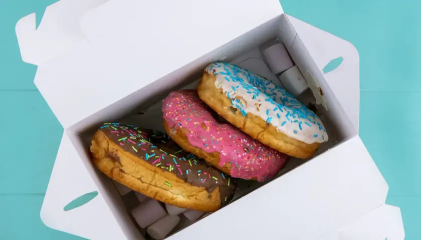Pyszne opakowanie cukiernicze z trzema kolorowymi donutami: czekoladowym, różowym i białym z niebieską posypką.