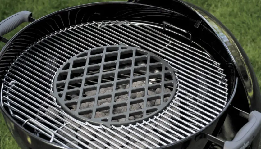Grill ogrodowy z rusztem i węglem drzewnym.