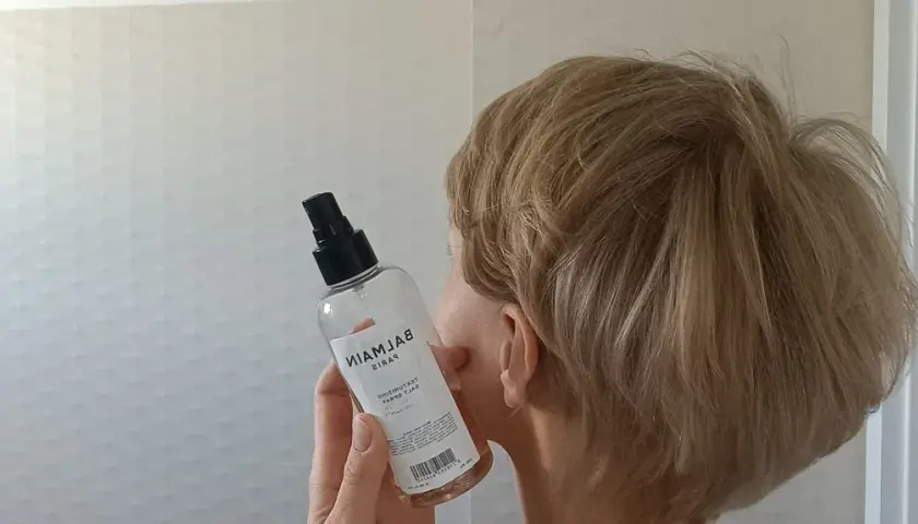 Kobieta z blond włosami trzyma butelkę z atomizerem, która zawiera sól morską do stylizacji włosów.