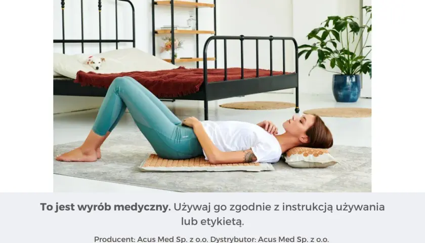 Kobieta leży na macie akupresurowej, która zapewnia masaż uda. W tle łóżko z psem.