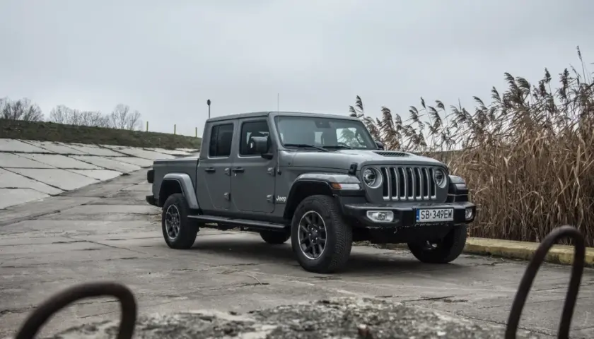 Szary Jeep Gladiator na betonowym podłożu, z suchymi trawami w tle.