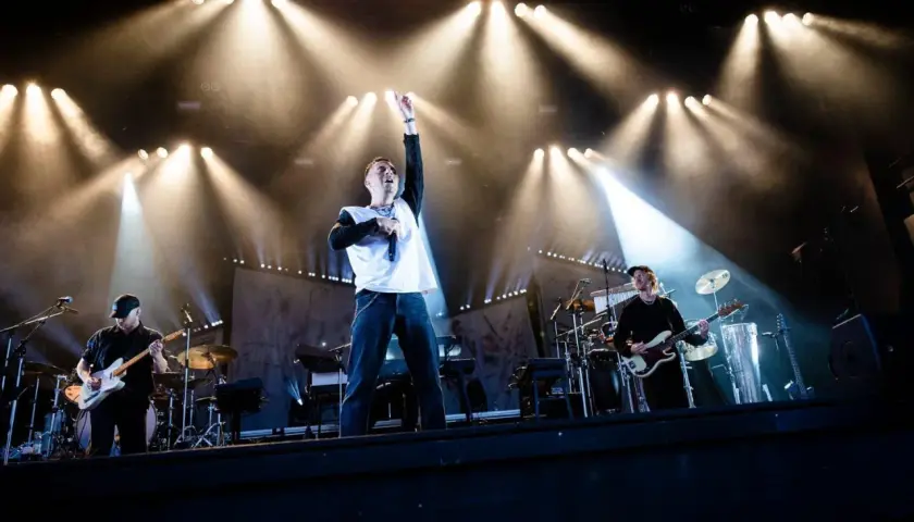 Oskar Linnros konsert med bandet upplyst av starka strålkastare. Sångaren med mikrofonen i handen och en arm uppsträckt.