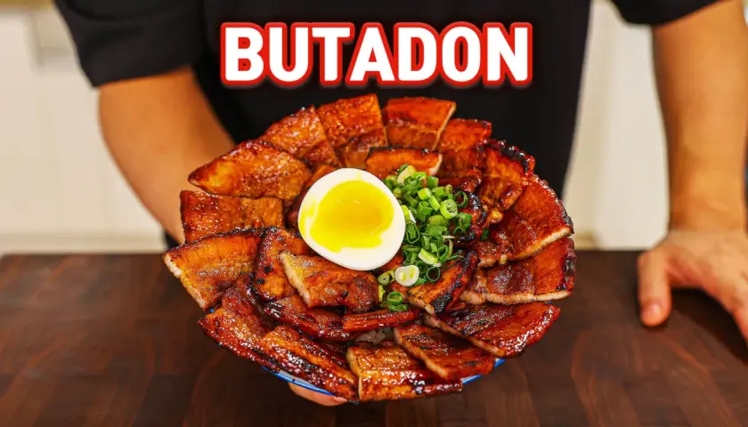 A generous serving of glistening pork donburi, topped with a perfectly soft-boiled egg and chopped green onions.