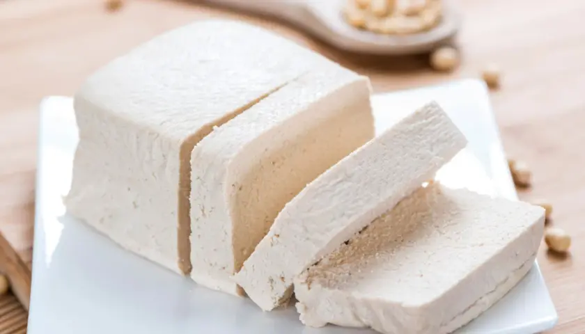 Kostka tofu, pokrojona w plastry, na białym talerzyku. Czy tofu to soja? Tak, to produkt z soi.