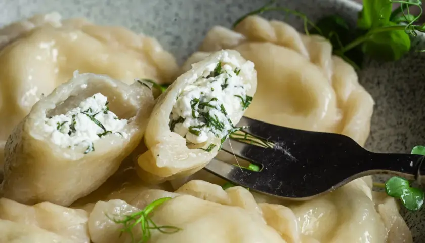 Pyszne pierogi z serem i zieloną natką, jeden uchwycony widelcem, gotowy do skosztowania.