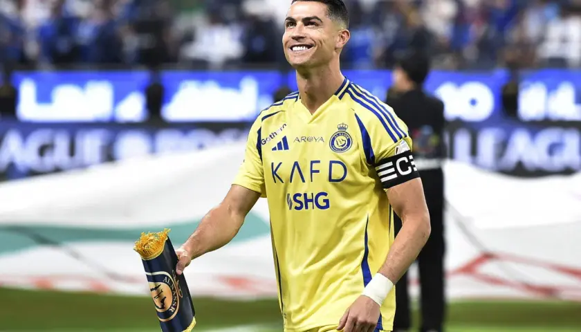 Uśmiechnięty Cristiano Ronaldo w żółtej koszulce Al Nassr, trzymający zwinięty szalik. Jego ogromne cristiano ronaldo zarobki budzą podziw.