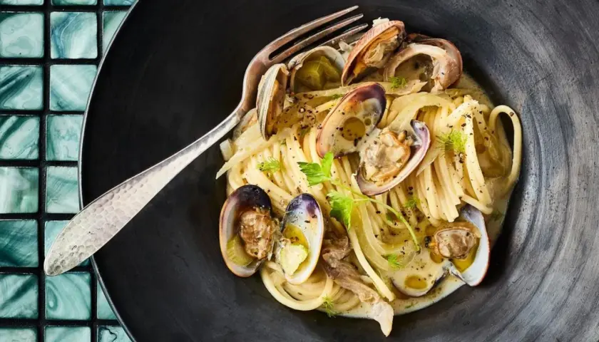 Spaghetti mit Venusmuscheln, ein köstliches Rezept. Serviert in einer schwarzen Schüssel mit einer Gabel.