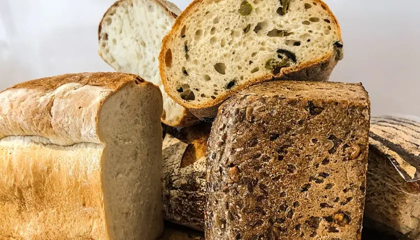 Variedad de panes artesanales, incluyendo un pan blanco esponjoso, un pan con aceitunas y un pan proteico con semillas.