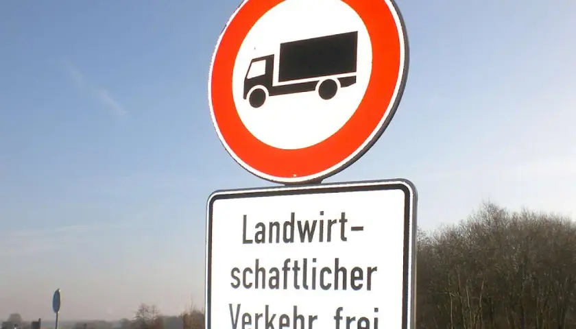 Verkehrsschild: LKW verboten, aber landwirtschaftlicher Verkehr frei. Blaue Himmel und Bäume im Hintergrund.