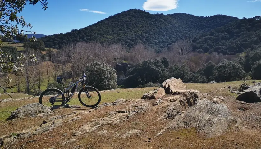 Bicicleta de montaña lista para explorar las **rutas en bici de montaña** en un paisaje rocoso y boscoso bajo un cielo azul.