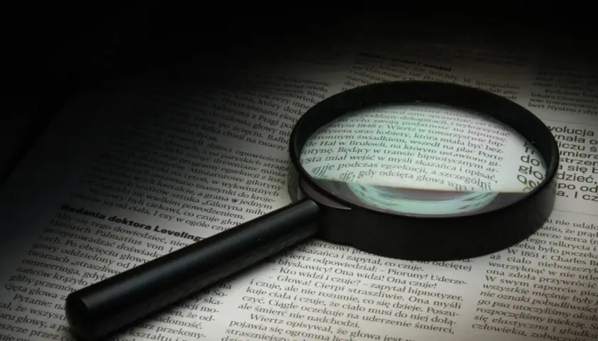 Lupa powiększa tekst, symbolizując dociekliwość i spostrzegawczość – kluczowe cechy dobrego detektywa.
