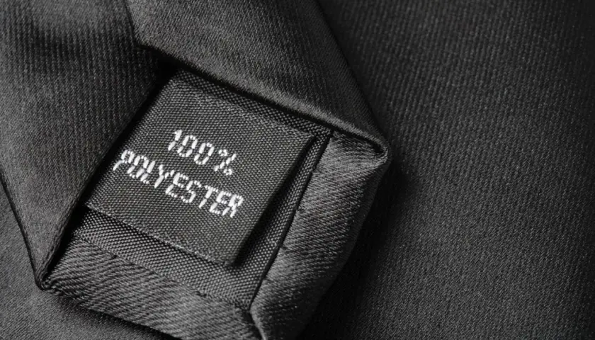 Czarna metka z napisem "100% POLYESTER" na tle eleganckiego materiału. Czy poliester jest zdrowy? To pytanie nurtuje wielu konsumentów.