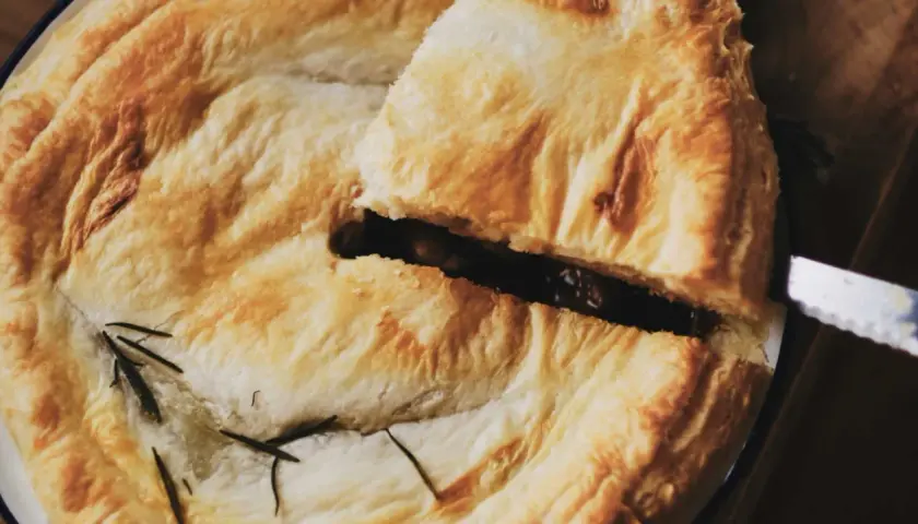 Un trozo de pastel con masa quebrada dorada, relleno oscuro y romero. Ideal para recetas con masa quebrada.