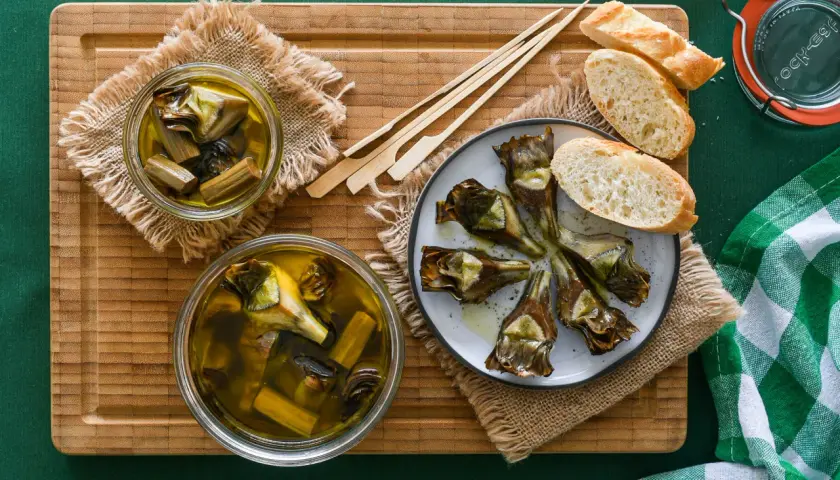 Deliciosas alcachofas confitadas en aceite de oliva, servidas con pan y palillos. Un manjar listo para disfrutar.