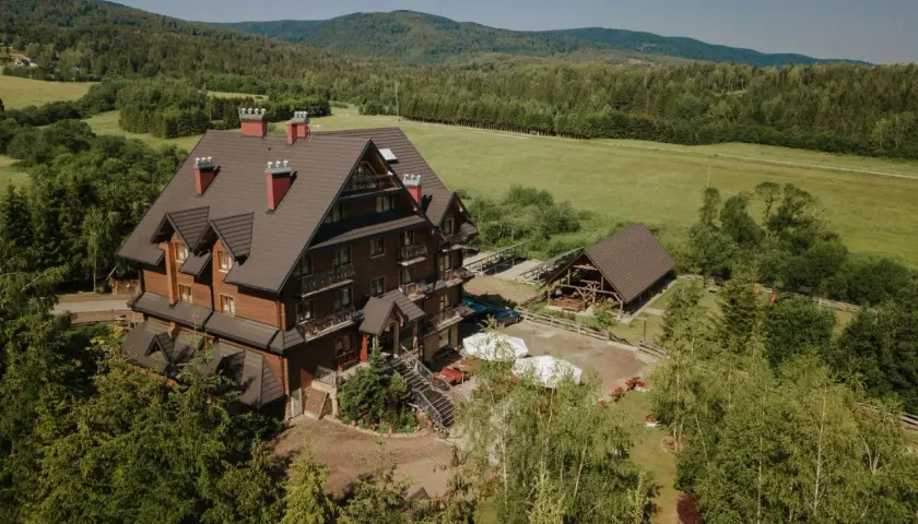 Hotel Carpatia Bieszczadzki Gościniec w otoczeniu zieleni, z drewnianym budynkiem i widokiem na góry.