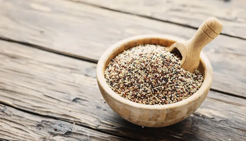 Ciotola di legno piena di quinoa tricolore, un legume nutriente, con un mestolo di legno.