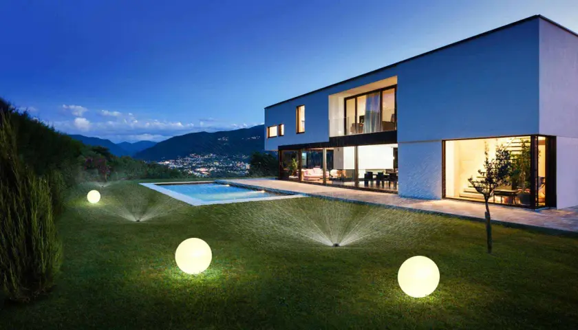 Modern villa con piscina iluminada y aspersores automáticos, un ejemplo de ideas domotica para un jardín perfecto.