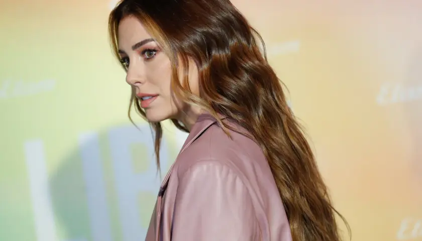 Mujer con cabello largo y ondulado, de color de pelo avellana con reflejos dorados, luciendo un traje rosa.