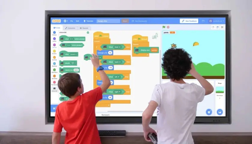 Zwei Kinder lernen Programmieren an einer digitalen Tafel in der Schule. Sie erstellen ein Spiel mit Scratch, das auf einem micro:bit basiert.