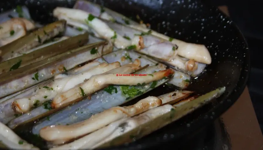 Longueirón de Fisterra cocinándose en una sartén con perejil picado. Un plato marinero listo para disfrutar.