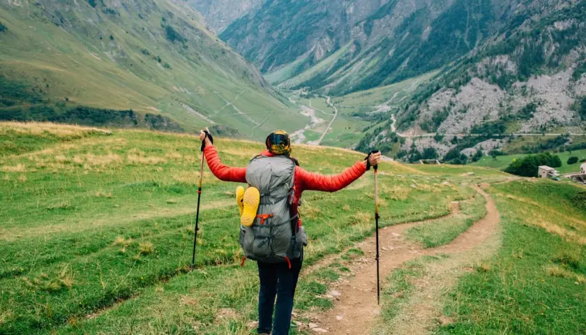 A hiker with a large backpack and trekking poles embraces the stunning alpine scenery on a self-guided tour du mont blanc.
