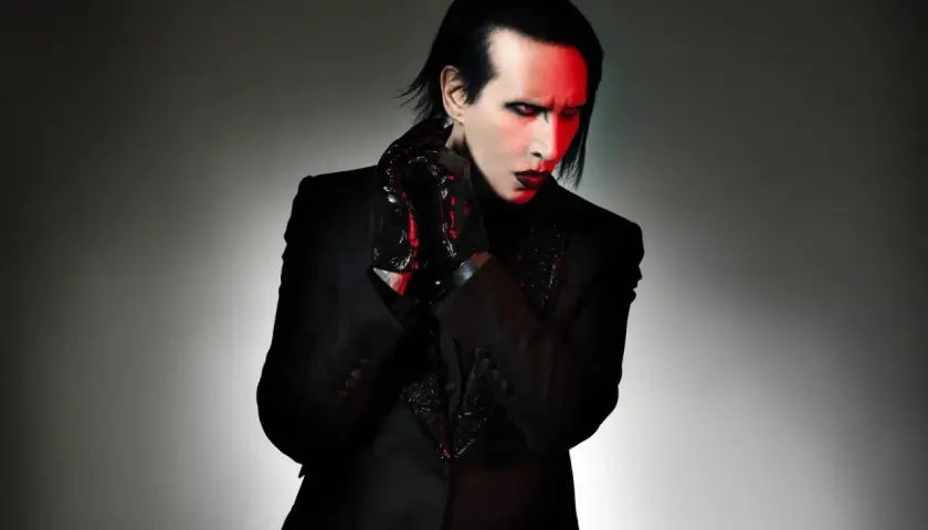 Marilyn Manson, wokalista zespołu, w czarnym garniturze i błyszczących rękawiczkach, z czerwonym światłem na twarzy.