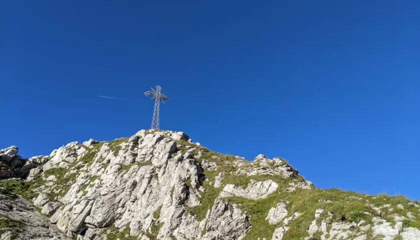 Kamienna ścieżka prowadzi pod górę, gdzie widać krzyż na szczycie. W oddali widać samolot. Kolejka na Giewont to wyzwanie dla każdego turysty.