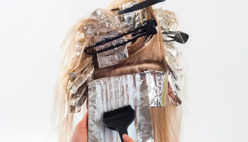 En frisör applicerar färg i slingor på blont hår, inslaget i folie. Kanske för att slinga håret gravid och känna sig extra fin.