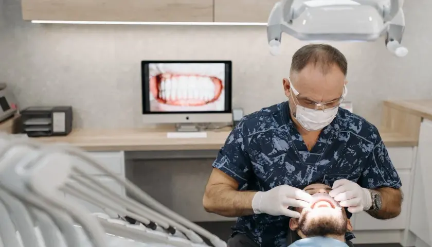 Dentysta w masce i rękawiczkach wykonuje zabieg, który może pomóc w usuwaniu kamienia nazębnego w domu. Na ekranie widać zbliżenie zębów.