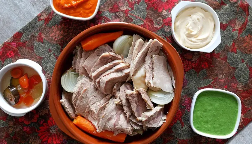 Un invitante bollito di carne, affettato e servito con carote, cipolle e tre salse: una rossa, una bianca e una verde.