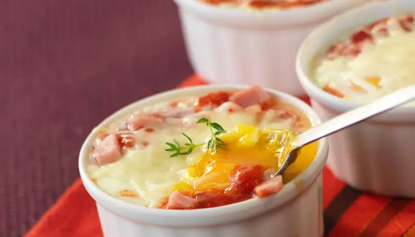 Œufs cocotte au four, jambon et fromage fondus, un délice crémeux prêt à être dégusté.