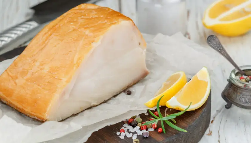 Un beau morceau de haddock fumé, prêt pour la cuisson, accompagné de quartiers de citron, de romarin et d'un mélange de poivre et de sel.