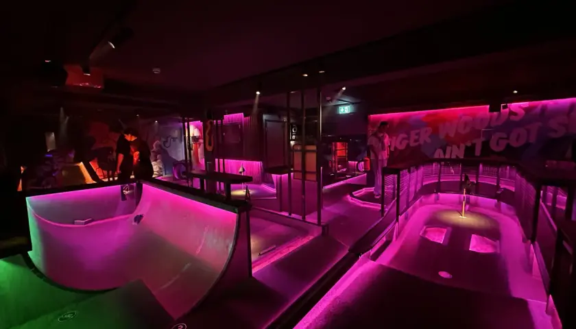 En neonupplyst minigolfbana i Göteborg med rosa och grönt ljus. En person står vid en bana.